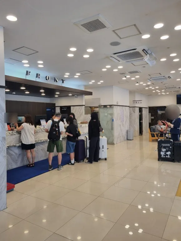 「FRONT」の表示がある東横INN釜山西面の受付カウンターと、スーツケースを持つ利用客。